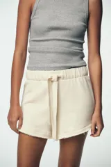 Shorts color crudo de tiro medio con cintura elástica ajustable con cordones y bajo desflecado.