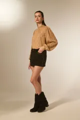 Minifalda marrón de gamuza sintética con tiro alto y detalles de tachas doradas a lo largo de los costados y bolsillos delanteros.