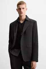 Blazer negro de lana con cuello de solapa de muesca, corte recto, manga larga con puños abotonados, bolsillos de vivo en el pecho y de solapa en la cadera, abertura en la parte posterior y cierre frontal con botones. Colección Origins.