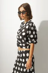 Blusa corta negra con estampado de lunares blancos, escote redondo, mangas abullonadas 3/4 y frunce central.