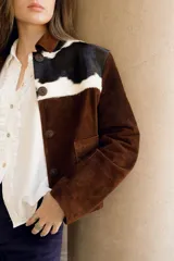 Chaqueta marrón de cuero vacuno con canesú delantero y trasero en cuero vacuno raza Holando (blanco con manchas negras), con cuello clásico, cierre frontal con botones y bolsillos laterales.