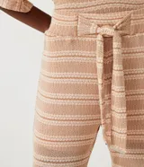 Pantalón largo de tejido de punto con rayas horizontales en tonos beige y marrón claro. El pantalón es de corte flare, con cintura alta y lazo para ajustar.