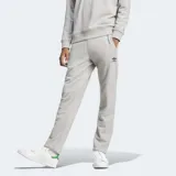 Pantalón de jogging Adidas Essentials Trifolio color gris melange, de corte ajustado, con cintura elástica y cordón ajustable. Incluye bolsillos laterales, puños acanalados y logo del trifolio bordado en negro en la pierna izquierda.