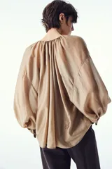 Blusa color dorado de lyocell con cuello redondo con cordón ajustable, abertura en V y mangas globo largas con puños vueltos con abertura y botón.