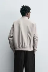 Cazadora bomber ligera gris confeccionada en tejido técnico. Cuello y puños en rib elástico, manga larga, bolsillos de vivo en cadera y bolsillo interior. Cierre frontal con cremallera.