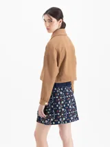 Chaqueta corta color marrón, sin forrar, confeccionada en sarga. Presenta doble cuello (mao interno y camisero externo), doble acceso frontal con cierre y broches, bolsillos plaqué con tapa y jareta con elástico y tancas metálicas. Las mangas tienen recortes y puños con broches.