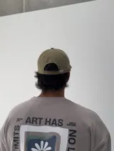 Gorro tipo gorra de béisbol color beige, con visera curva y estampado frontal con la palabra "HUDSUN" en naranja y blanco, y texto "It all started here 1975 sunset flower".