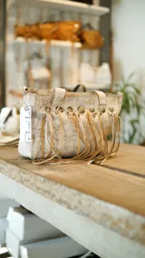 Cartera de cuero color crema con textura craquelada, doble asa corta y flecos de cuero en el frente.