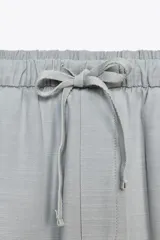 Pantalón culotte color crudo, de tiro medio, cintura elástica ajustable con cordones y bolsillos laterales ocultos en la costura.