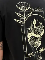 Remera negra de algodón con cuello redondo y mangas cortas. Estampado en la espalda con diseño de serpiente enroscada en rosas y texto 'On Tour 1990 Originals Co.'.
