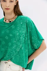Remera holgada de color lila con estampa de motivos bandani y cruce doble en el frente.