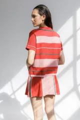 Remera polo tejida a rayas horizontales rojas y rosadas, con cuello clásico y bordado de ají verde.