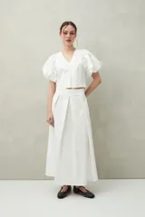 Falda midi blanca con pequeños lunares negros, de corte acampanado y cintura alta con pliegues.