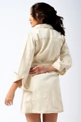 Vestido camisero corto de denim azul oscuro, con cuello clásico, mangas 3/4 con puños abotonados, cierre frontal con botones color cobre, cinturón de lazo y bolsillos con solapa en el pecho.