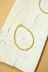 Pulsera elástica de cristal facetado color verde claro, con dije de bolita cubierta de circonias y detalles en dorado.