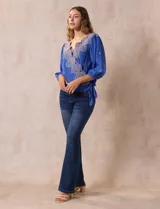Blusa azul con bordados color crema, escote en V cruzado, mangas 3/4 abullonadas y nudo en el ruedo.