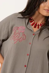 Camisa verde de silueta oversize con cuello camisero y manga 3/4. Tiene bordados de coral y caracol en el frente y botones a tono.