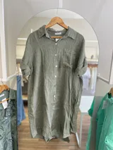 Vestido camisero corto color verde oliva, confeccionado en lino. Tiene cuello camisero, mangas cortas con trabillas y botones, y un bolsillo de parche en el pecho.