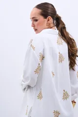 Camisa blanca de manga larga con bordado de hojas doradas.