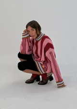 Sweater de punto oversize a rayas verticales rosas y bordó, con cuello alto y puños con ribete celeste.