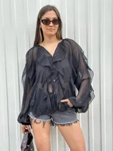 Blusa negra traslúcida con volados, mangas largas abullonadas y cierre frontal con botones.