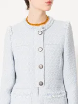 Chaqueta corta de jacquard chanel color celeste, con cuello redondo y cierre frontal con botones marrones. Presenta detalles de flecos en el escote, bolsillos delanteros inferiores y sisas.
