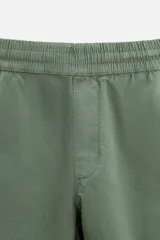 Bermuda color verde militar de corte relajado, confeccionada en tejido de algodón. Tiene cintura elástica ajustable con cordón interior, bolsillos frontales y bolsillo trasero de parche.