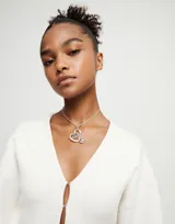 Colgante de aleación de metales con baño en plata de ley, con dije en forma de corazón estilizado que contiene un cristal facetado de color gris oscuro. La cadena es fina y plateada, con cierre de mosquetón y extensión ajustable.