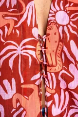 Blusa oversize de poliéster con estampado de animales y plantas en tonos rosa y marrón. Tiene cuello camisero, mangas largas y cierre frontal con lazos.