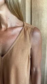 Vestido largo color crudo, sin mangas y con escote en V. Presenta aberturas laterales en el ruedo y bolsillos laterales a la altura de la cadera.