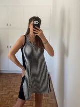 Vestido corto sin mangas, de silueta amplia y calce relajado. El frente es de tejido a rayas horizontales blancas y negras, mientras que los laterales son lisos en color negro. Posee escote redondo.