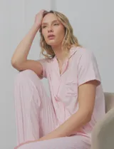 Conjunto de pijama marca Pillow Talk, compuesto por camisa de mangas cortas con solapa y bolsillo, y pantalón largo con cintura elastizada y lazo de ajuste. Diseño a rayas verticales rosas y blancas.