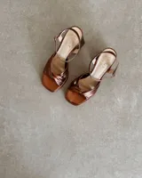 Sandalia de cuero vacuno color dorado, con plataforma y taco cuadrado. Presenta una tira delgada en el tobillo y detalle de nudo en la capellada.