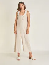 Mono de lino color beige, con pierna ancha y largo a media pantorrilla. Tiene escote cuadrado, breteles anchos en color blanco y cierre invisible en la espalda. Incluye lazo blanco para ajustar en la cintura.