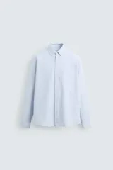 Camisa celeste de corte regular fit, confeccionada en tejido de algodón. Tiene cuello abotonado, manga larga con puños abotonados, bolsillo en el pecho y cierre frontal con botones.