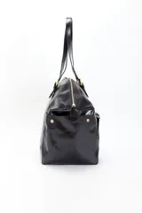 Bolso tote grande de cuero negro con herrajes dorados. Tiene bolsillos tipo guantera y con cierre. El interior está forrado en gabardina con un bolsillo interno. Se accede al interior mediante un cierre metálico.