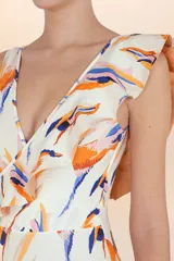 Traje de baño entero blanco con estampado abstracto en tonos naranja, azul y rosado. Presenta escote en V cruzado y un volado asimétrico que cae sobre un hombro.