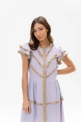 Vestido midi lila con volados en las mangas y detalles de ribete en color beige que forman patrones en zigzag en el torso. Presenta un frente abotonado con tapeta beige.