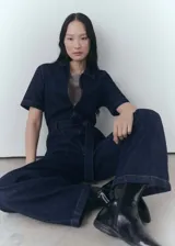Mono largo de denim azul oscuro, con cuello camisero, mangas cortas y cierre frontal con cremallera. Incluye cinturón ajustable, bolsillos laterales y trabillas.