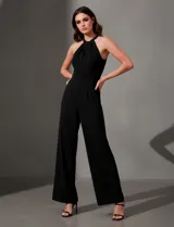 Enterito largo de crepe color negro, con escote halter entrelazado y piernas anchas. Presenta bolsillos delanteros y abertura en la espalda con cierre invisible y botón.