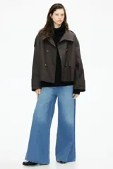 Gabardina corta color marrón chocolate, de corte holgado, con cuello clásico, doble botonadura, charreteras, trabillas abotonadas en los puños, bolsillos delanteros con solapa y pliegue invertido en la espalda. Forrada.