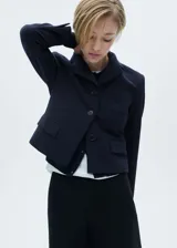 Blazer azul marino con cuello de pico y solapa, diseño crop, bolsillo de parche en el pecho, manga larga con puños abotonados, diseño recto y dos bolsillos de solapa en la parte delantera.