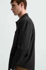 Sobrecamisa negra de tejido con elasticidad, cuello solapa, manga larga con puño abotonado, bolsillos de plastrón en el pecho y cierre frontal con botones a presión.