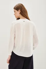 Camisa blanca de manga larga con cuello mao y escote en V. Presenta bordados florales en blanco y dorado en el frente.