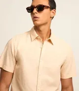Camisa color beige claro de lino y algodón, corte comfort, manga corta, cuello camisero, cierre con botones y sin estampa.