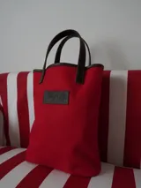 Bolso matero de lona color azul con detalles en cuero marrón, con asas cortas y logo de la marca en cuero.