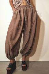 Pantalón bombacho marrón de tejido fluido, tiro medio con cintura elástica ajustable con cordones, bolsillos laterales ocultos y bajo abullonado con elástico interior.