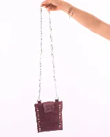Porta celular de cuero color bordó con correa de cadena plateada, solapa con broche y tachas plateadas en los bordes.