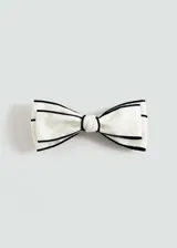 Accesorio para el pelo tipo pasador con forma de moño color blanco con bordes negros. Tiene cierre metálico a presión.
