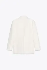 Blazer blanco de corte oversize, con cuello solapa, manga larga con hombreras, bolsillos de doble vivo en el delantero, aberturas en la espalda y cierre cruzado con botones.